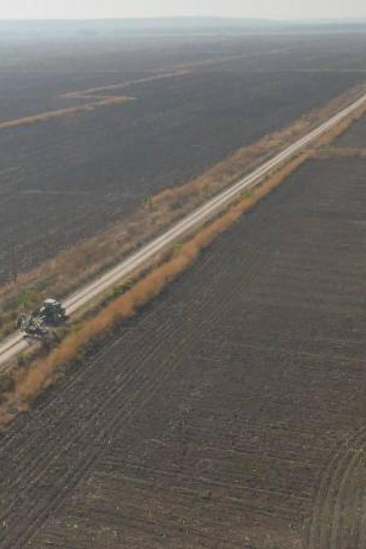 Ein Traktor fährt auf einem Feldweg durch eine weite, braune Ackerlandschaft.