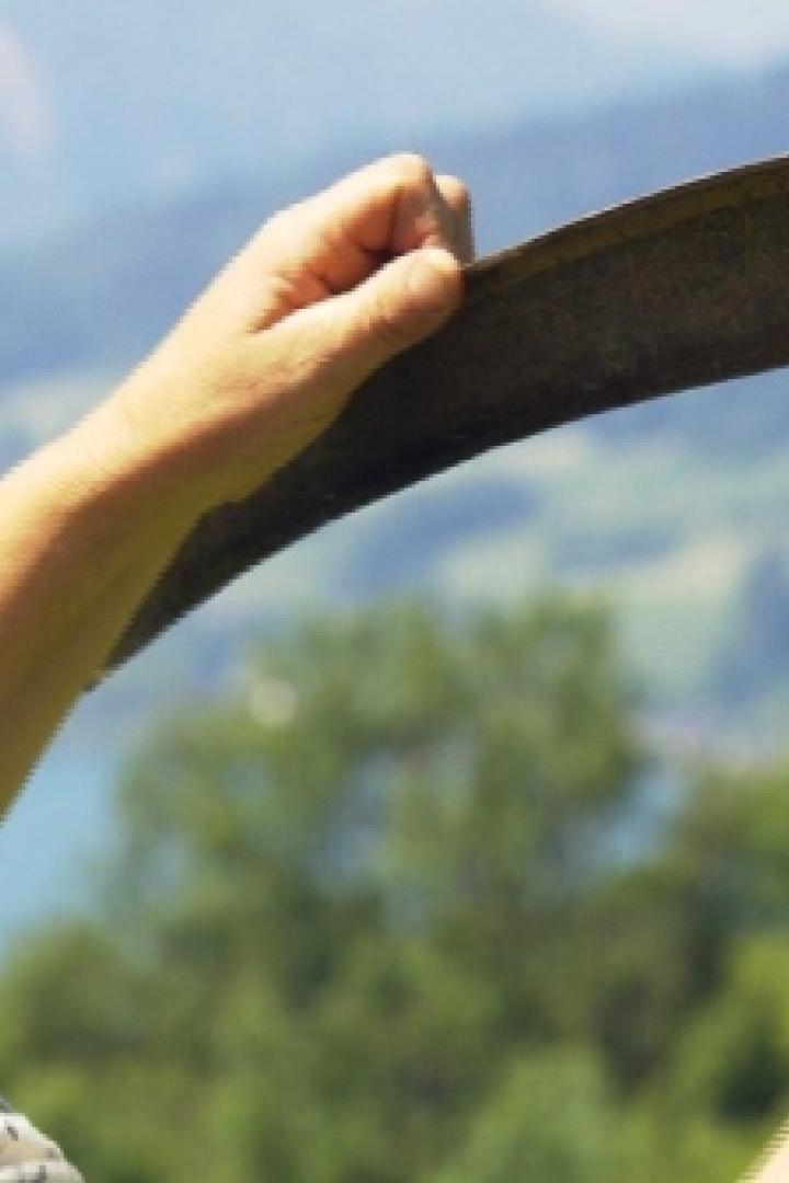 Eine Frau inspiziert eine Sense vor einer grünen Landschaft.