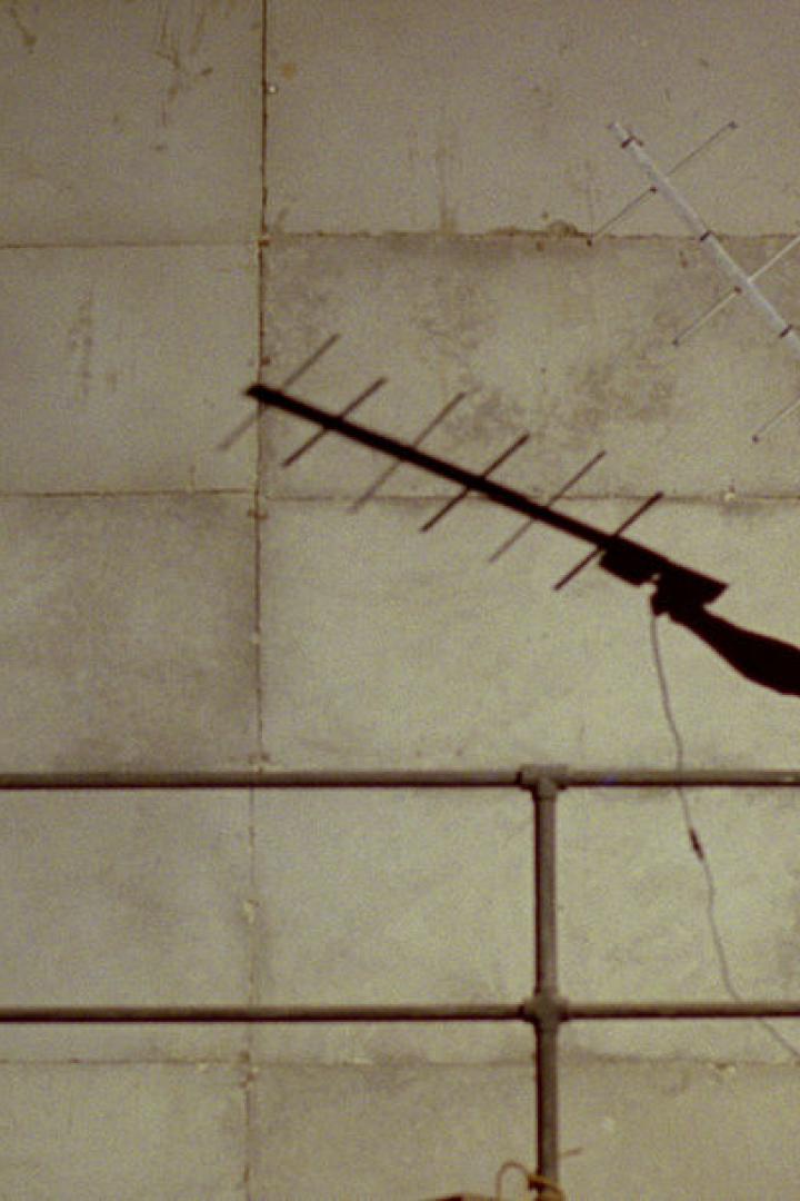 Ein Mann mit Kopfhörern und Sonnenbrille hält eine Antenne vor einer großen Wand.