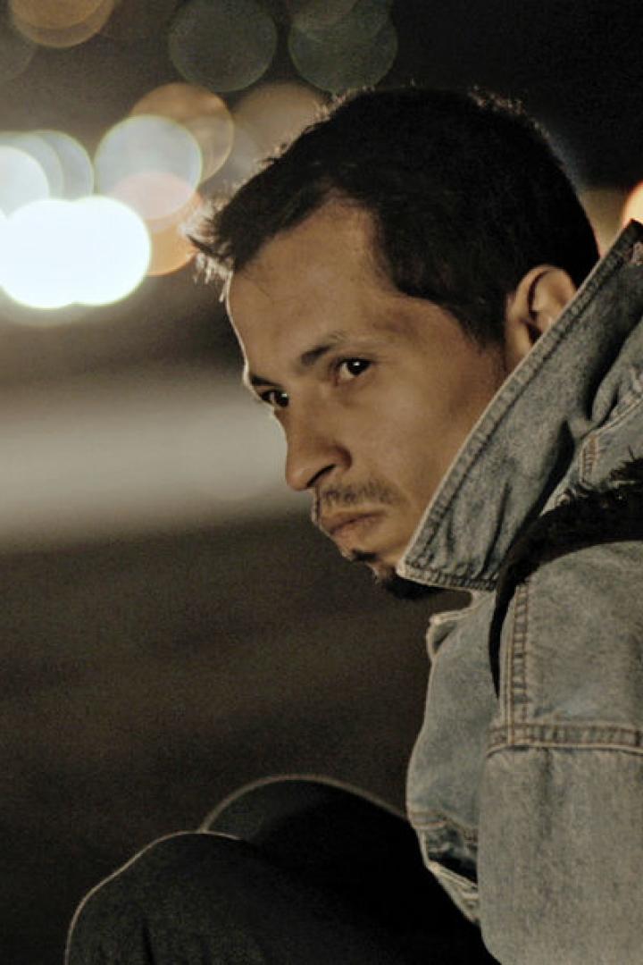 Ein Mann mit Jeansjacke und Rucksack sitzt nachts an einer Straße.