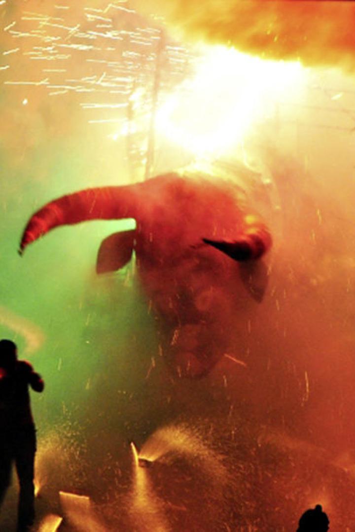 Menschen nehmen an einem Correfoc-Feuerlauf mit einem Stierkopf teil.