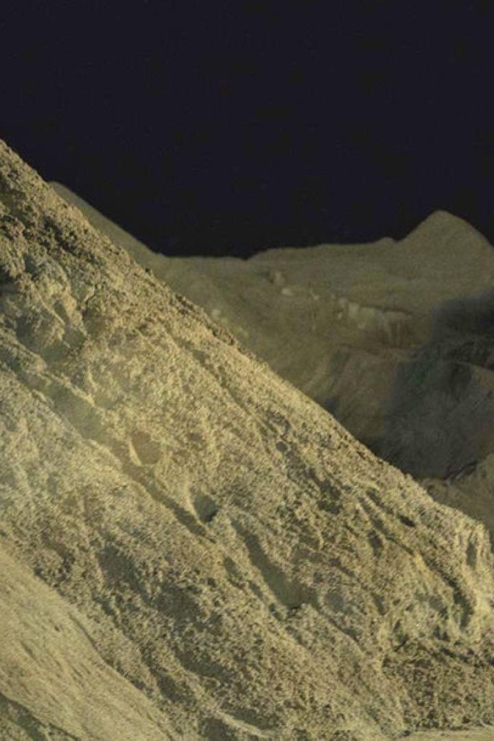 Eine Person steht vor großen Sandbergen und leuchtet mit einer Taschenlampe.