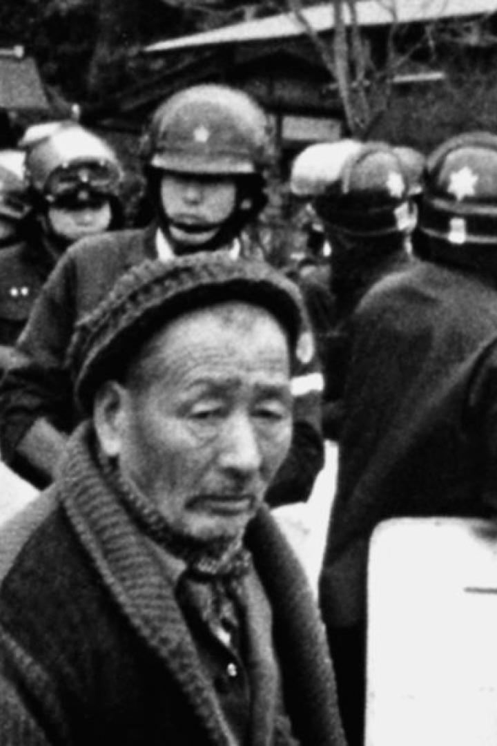 Ein älterer Mann steht vor einer Reihe von Polizisten mit Schutzschilden.