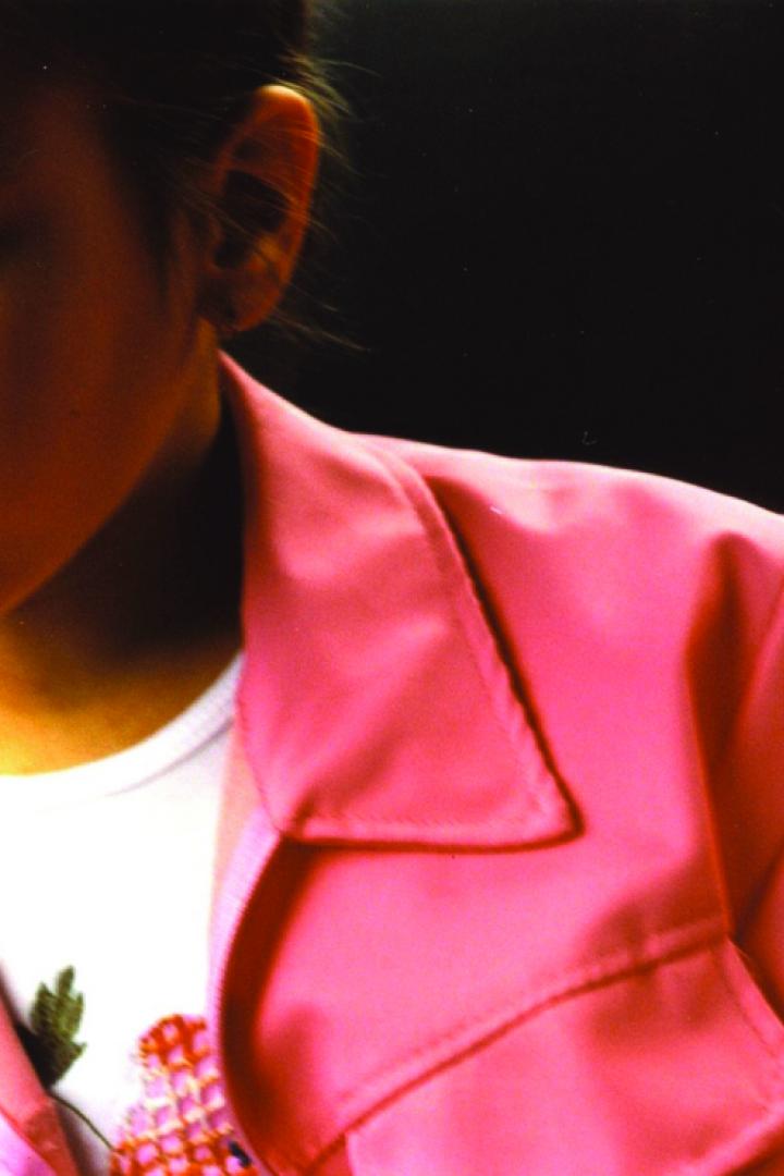 Ein junges Mädchen mit rosa Jacke schaut nachdenklich zur Seite.