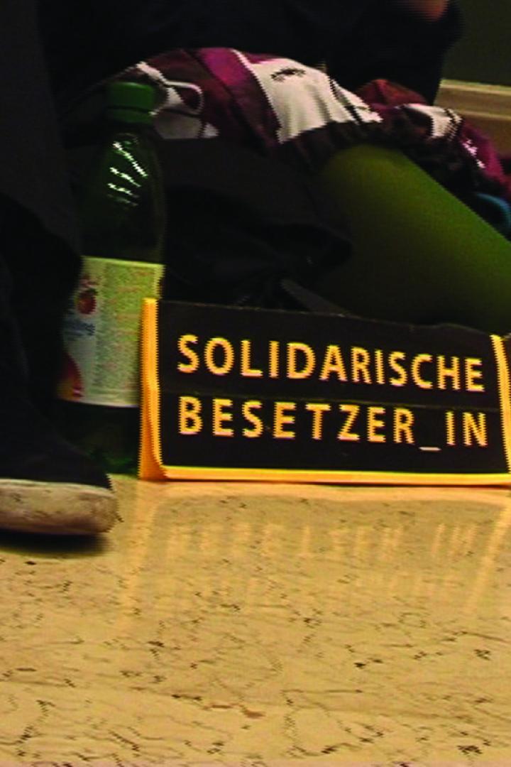 Ein Schild mit der Aufschrift „Solidarische Besetzer_in“ steht auf dem Boden.