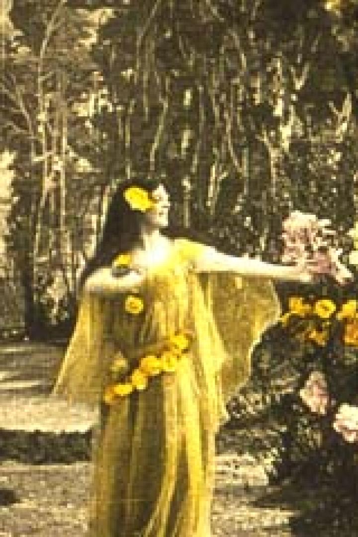 Eine Frau in einem gelben Kleid tanzt vor einem mit Blumen geschmückten Hintergrund.