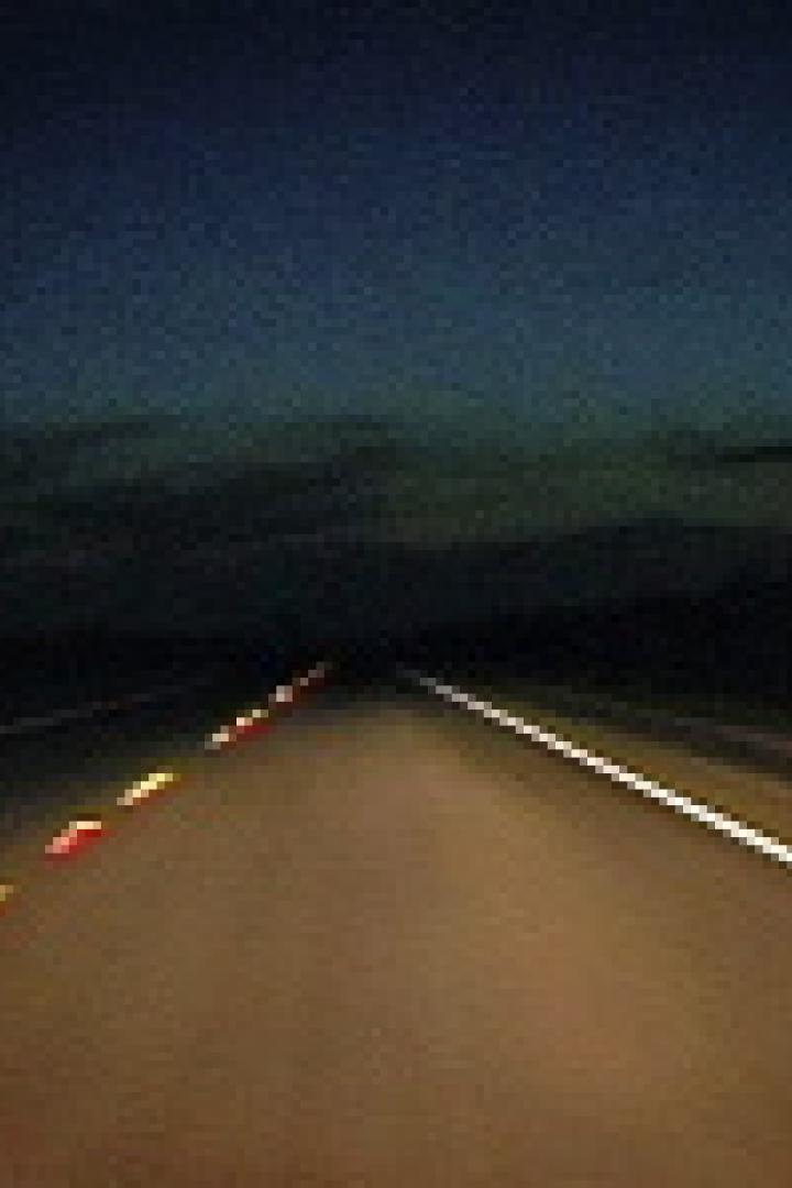 Eine dunkle Landstraße in der Nacht mit gelben und weißen Fahrbahnmarkierungen.