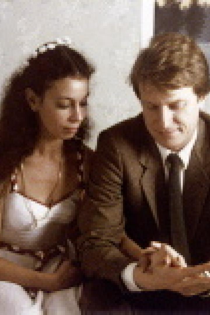 Ein Mann im Anzug und eine Frau im weißen Kleid sitzen nebeneinander.