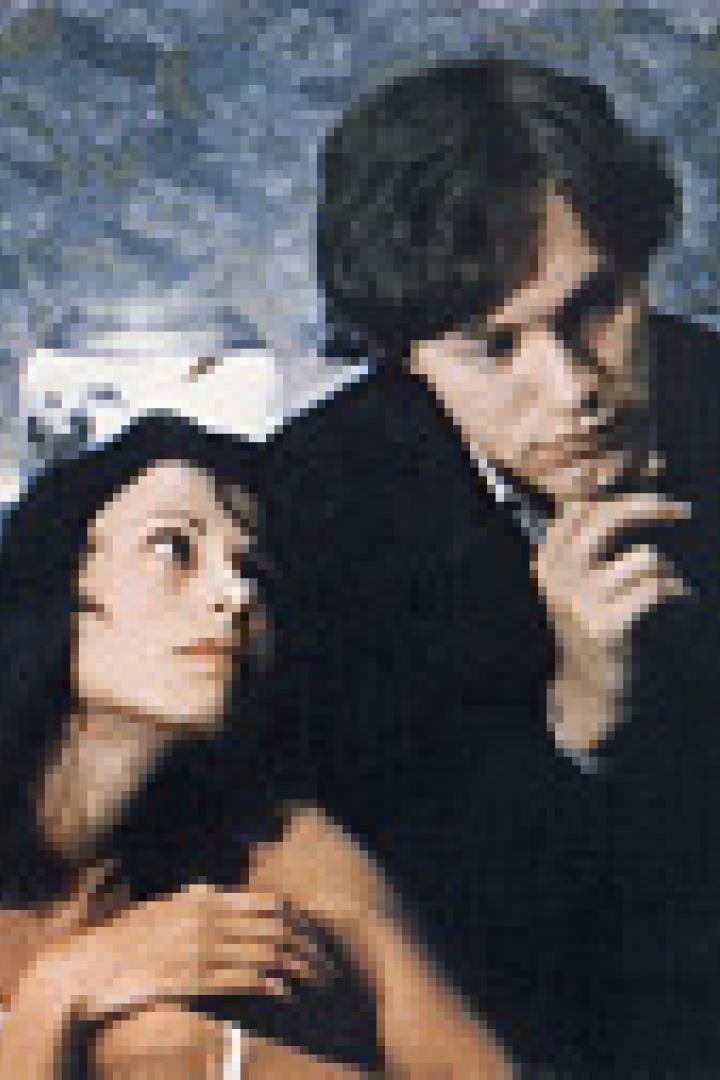 Eine Frau im Unterhemd und ein Mann im Anzug sitzen auf einem Bett.