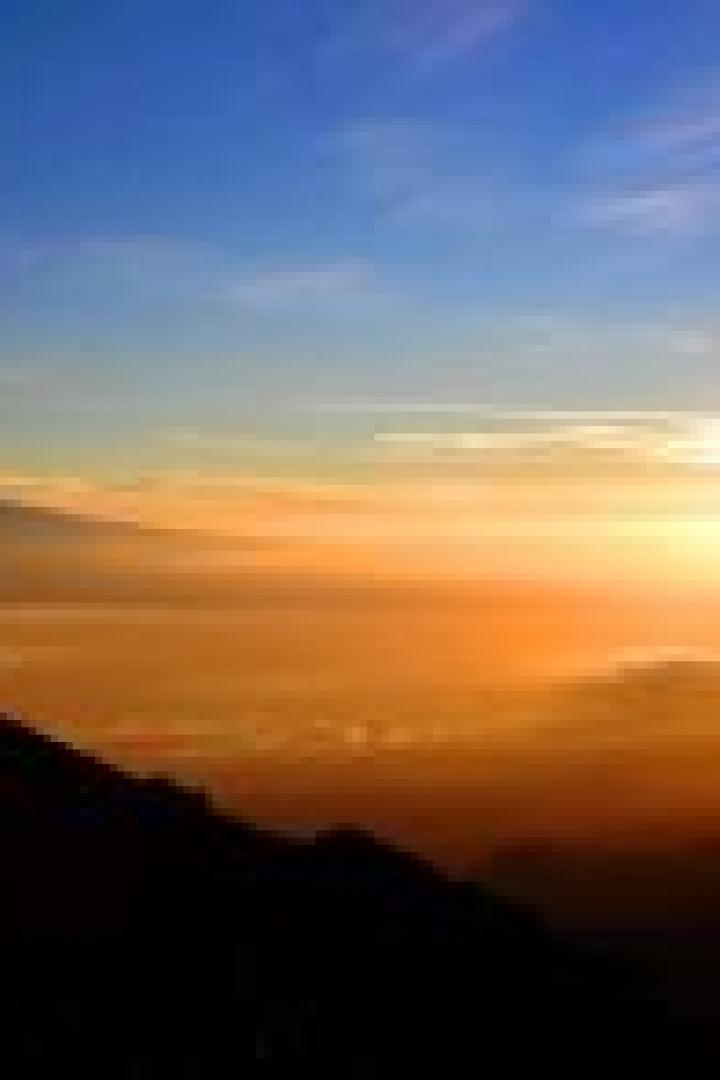 Eine Person steht auf einem Hügel und blickt auf den Sonnenaufgang über den Wolken.