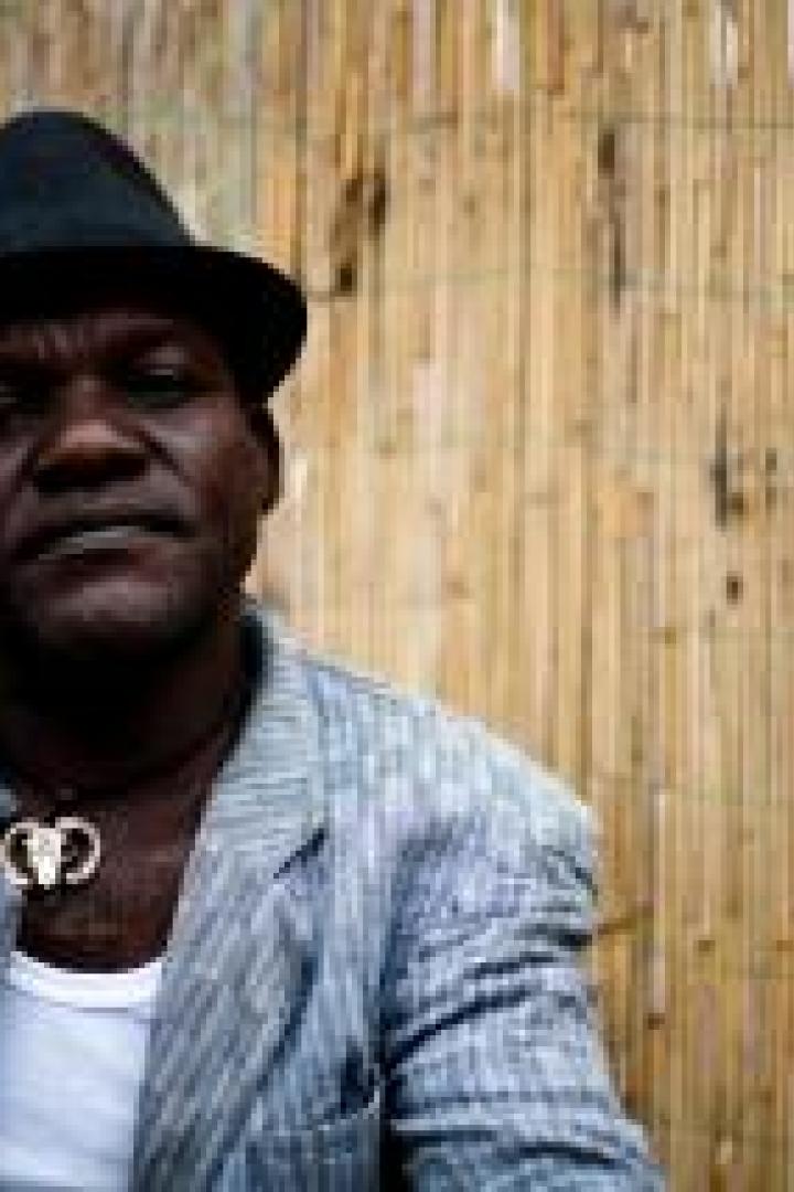 Ein Mann mit Hut hält eine Dose in der Hand, neben ihm eine Gitarre.