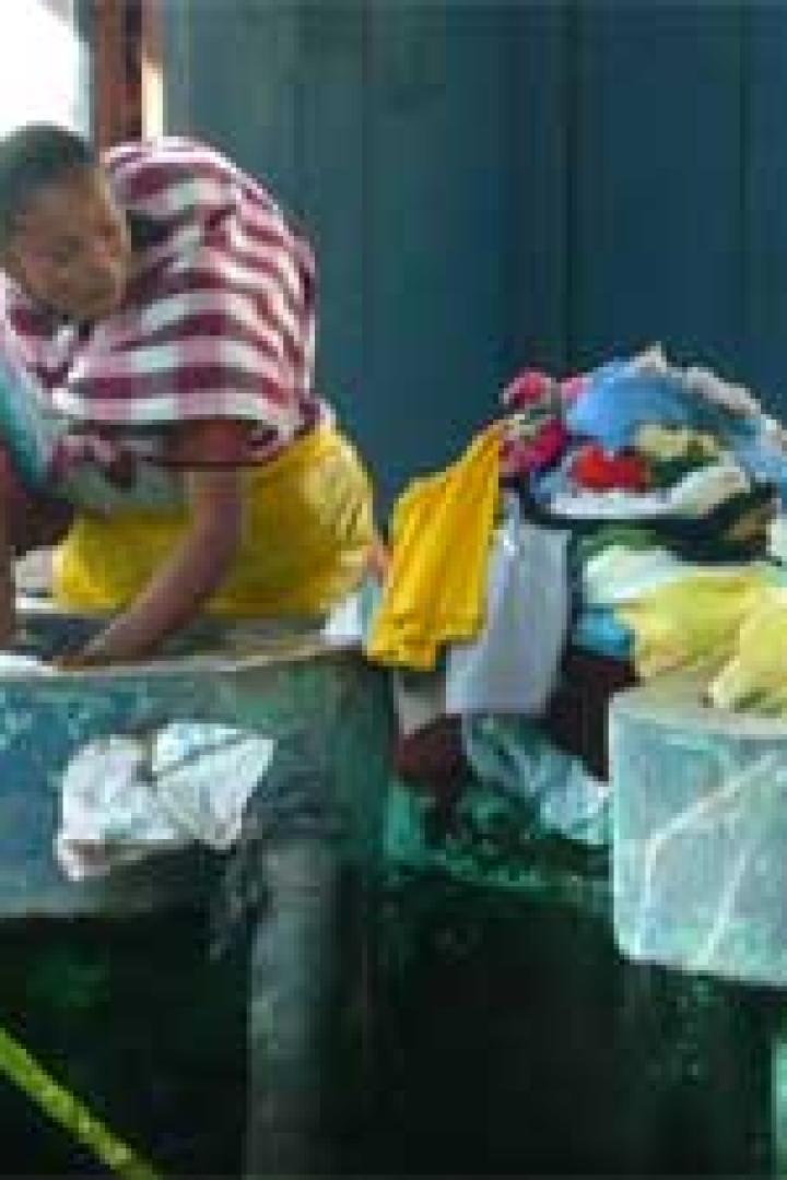 Eine Frau wäscht Kleidung in einem Waschbecken im Freien.