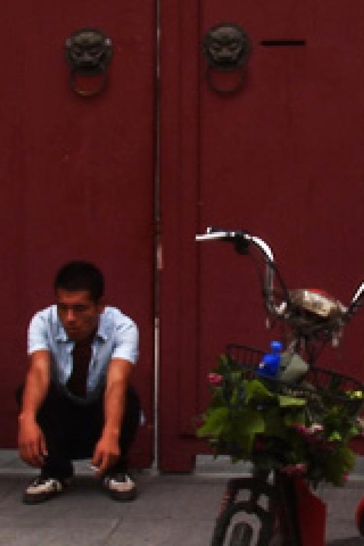 Ein Clown und ein Mann hocken vor einem roten Tor neben einem geschmückten Fahrrad.