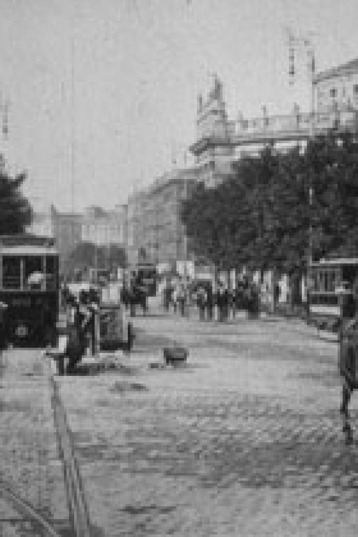 Eine belebte Straße mit Straßenbahnen und Pferdekutschen in einer Stadt um die Jahrhundertwende.