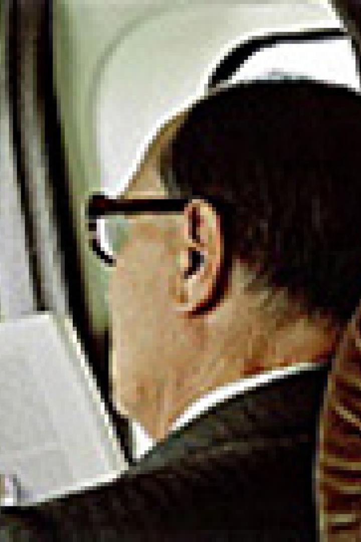 Ein Mann mit Brille liest ein Buch im Flugzeug.
