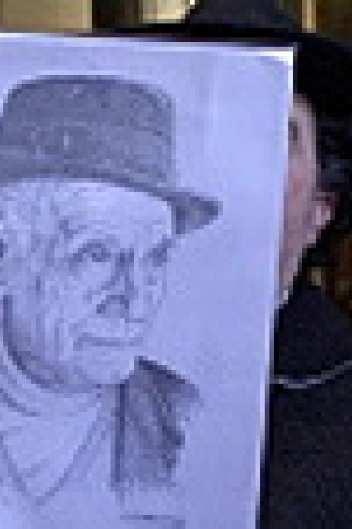 Eine Person hält eine Zeichnung eines älteren Mannes mit Hut vor ihr Gesicht.