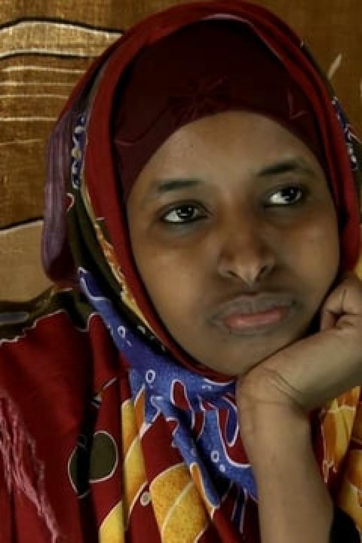 Eine Frau mit Kopftuch und gemustertem Schal stützt ihr Kinn auf ihre Hand.