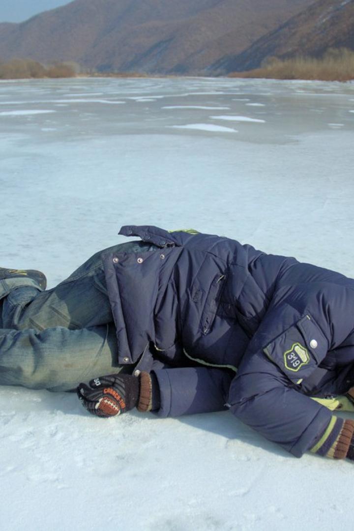 Ein Junge liegt auf einem zugefrorenen See, im Hintergrund sind Berge zu sehen.
