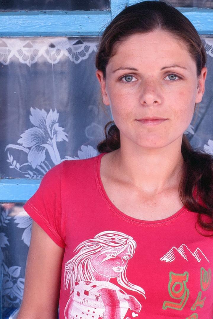 Eine junge Frau mit roten T-Shirt steht vor einem blau gestrichenen Fenster.