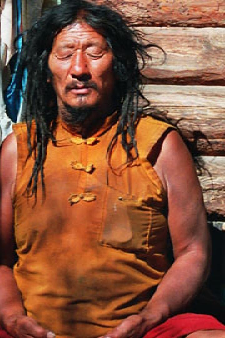 Ein Mann mit Dreadlocks meditiert vor einer Holzwand.