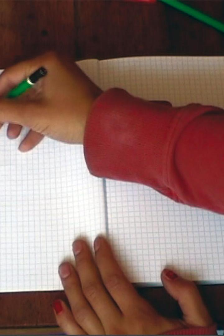 Eine Person zeichnet mit einem grünen Stift ein Gesicht in ein Notizbuch.