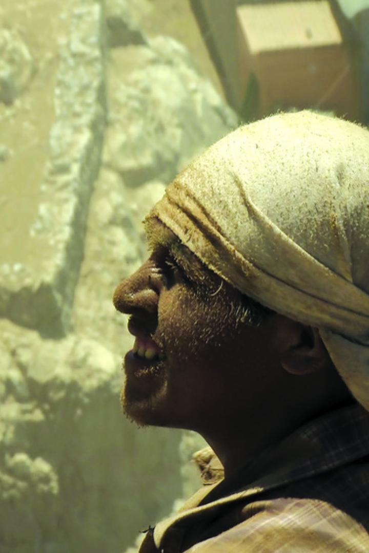 Ein Mann mit Kopftuch steht vor einer staubigen Felswand.