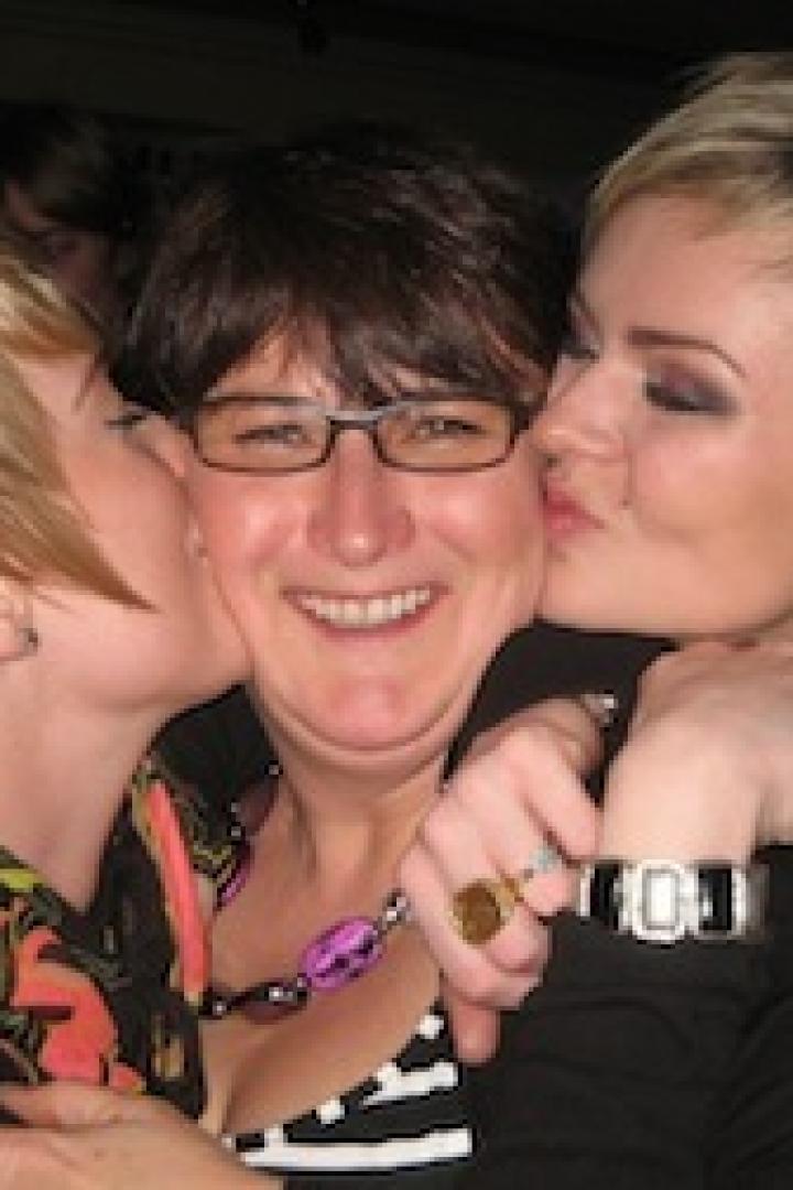 Zwei Frauen geben einer Frau mit Brille einen Kuss auf die Wange.