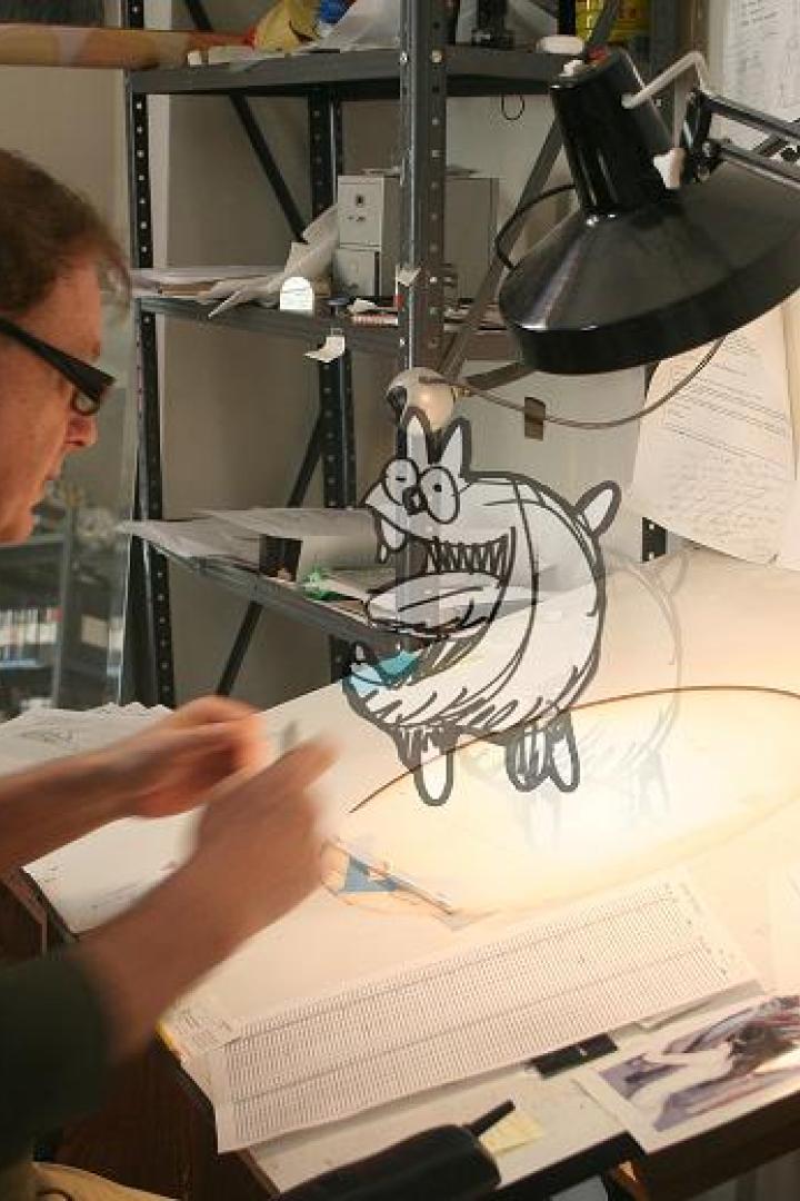 Ein Mann mit Brille arbeitet an einem Zeichentisch mit einer Cartoon-Zeichnung.