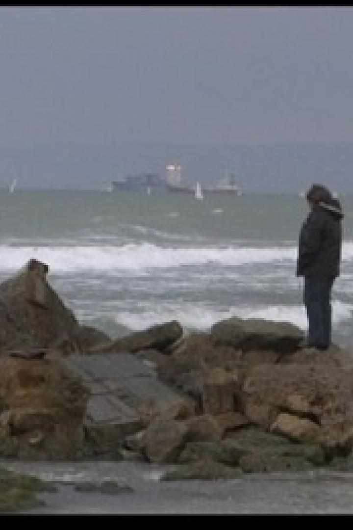Eine Person steht auf Felsen am Ufer und blickt auf das stürmische Meer.