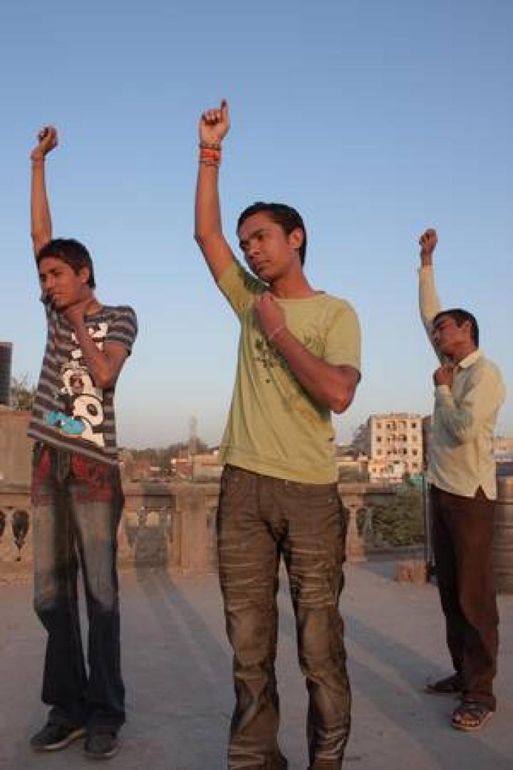 Drei junge Männer stehen auf einem Dach und heben die Arme.