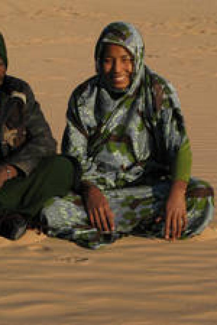 Zwei Frauen sitzen in traditioneller Kleidung in einer Wüste.