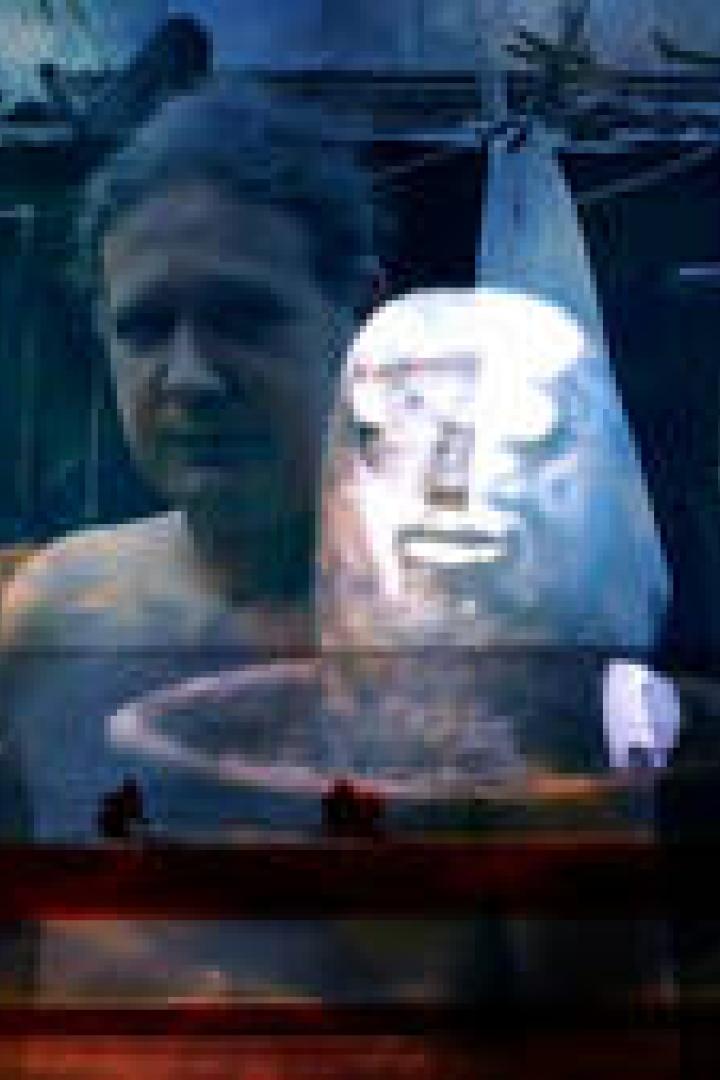 Ein Mann steht hinter einer silbernen Maske in einer dunklen Umgebung.