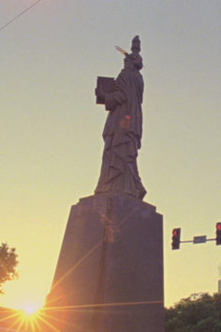 Eine Statue, die an die Freiheitsstatue erinnert, steht bei Sonnenuntergang in einer Stadt.