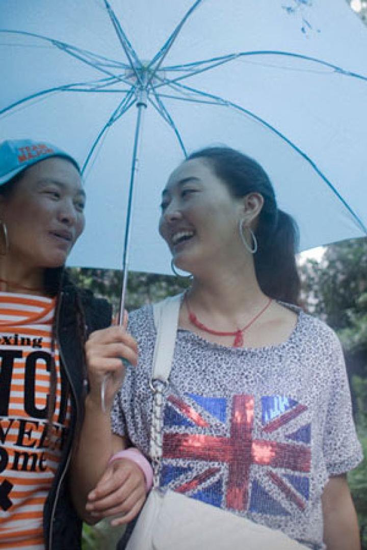 Zwei Frauen stehen unter einem blauen Regenschirm und lächeln sich an.