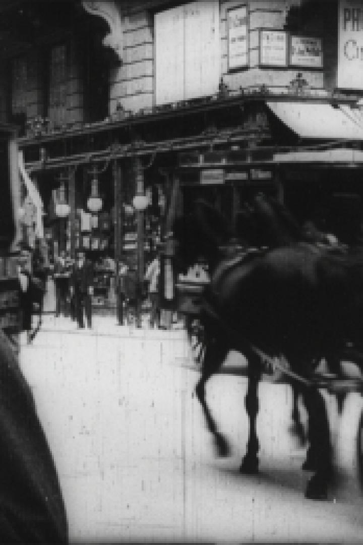 Eine belebte Straße mit einer Pferdekutsche und Passanten in einer historischen Aufnahme.