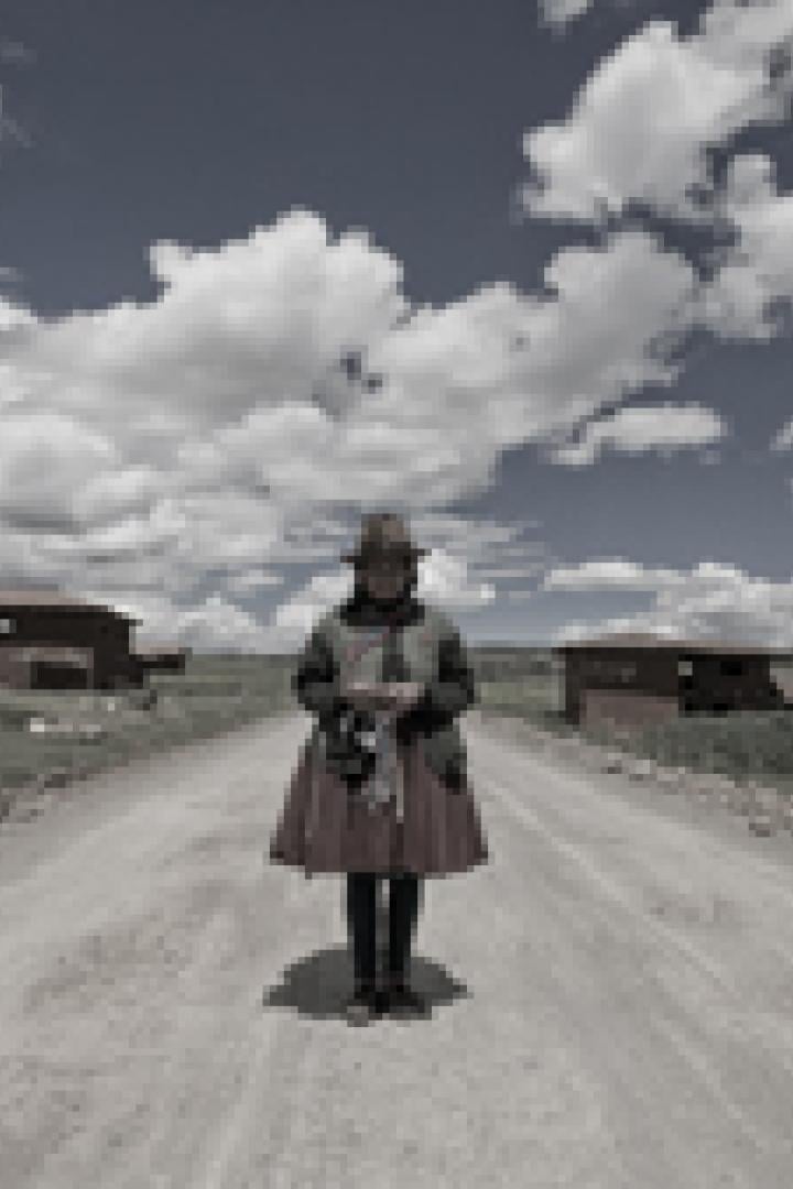 Eine Frau in traditioneller Kleidung steht auf einer Landstraße vor einer ländlichen Szenerie.