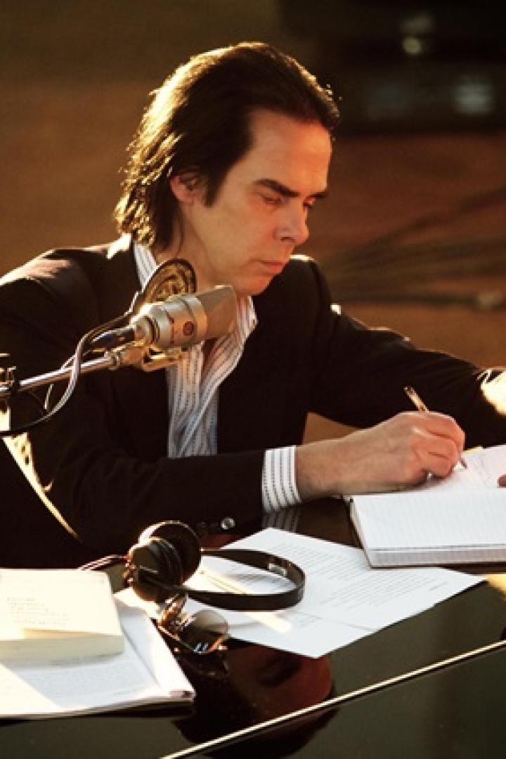 Nick Cave sitzt am Klavier und schreibt in ein Notizbuch.