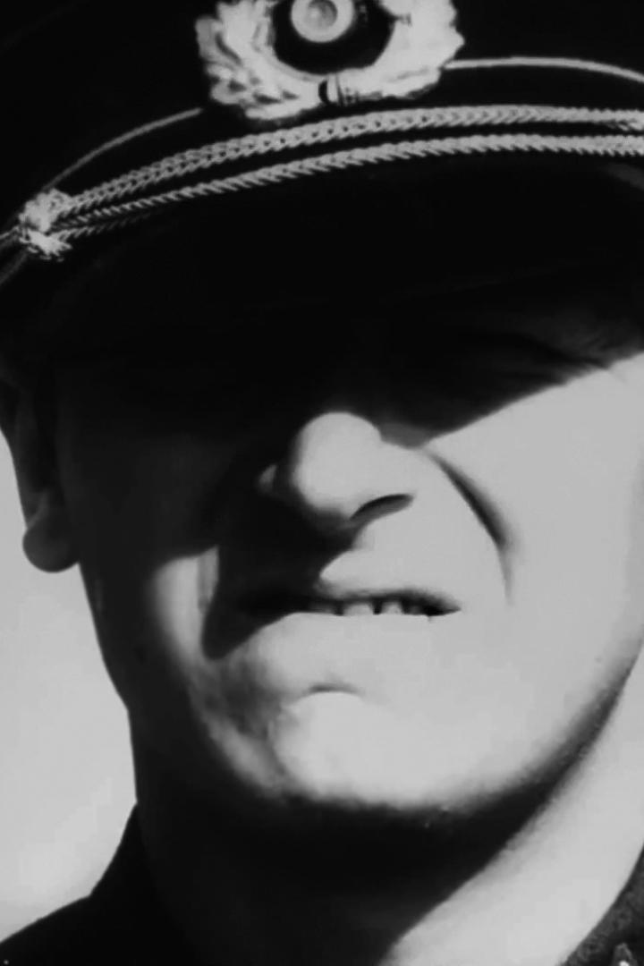 Ein Mann mit Uniformmütze, dessen Gesicht im Schatten liegt.