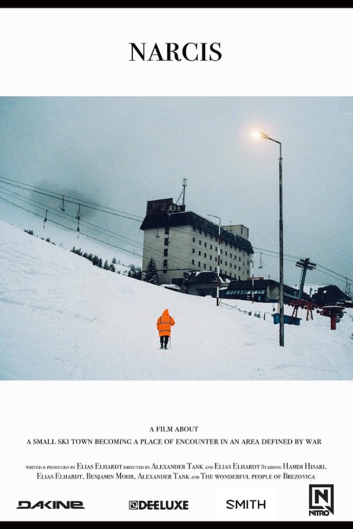 Ein Mann in oranger Jacke geht auf ein Hotel in einem verschneiten Skiort zu.