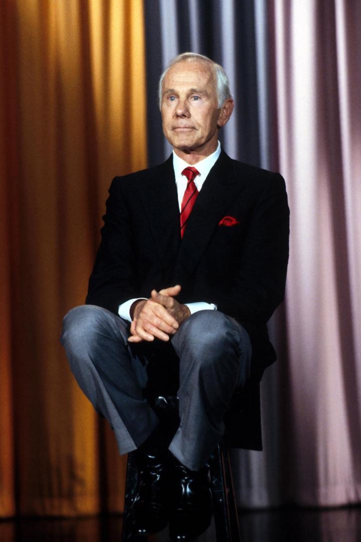 Johnny Carson sitzt auf einem Stuhl vor einem Vorhang.