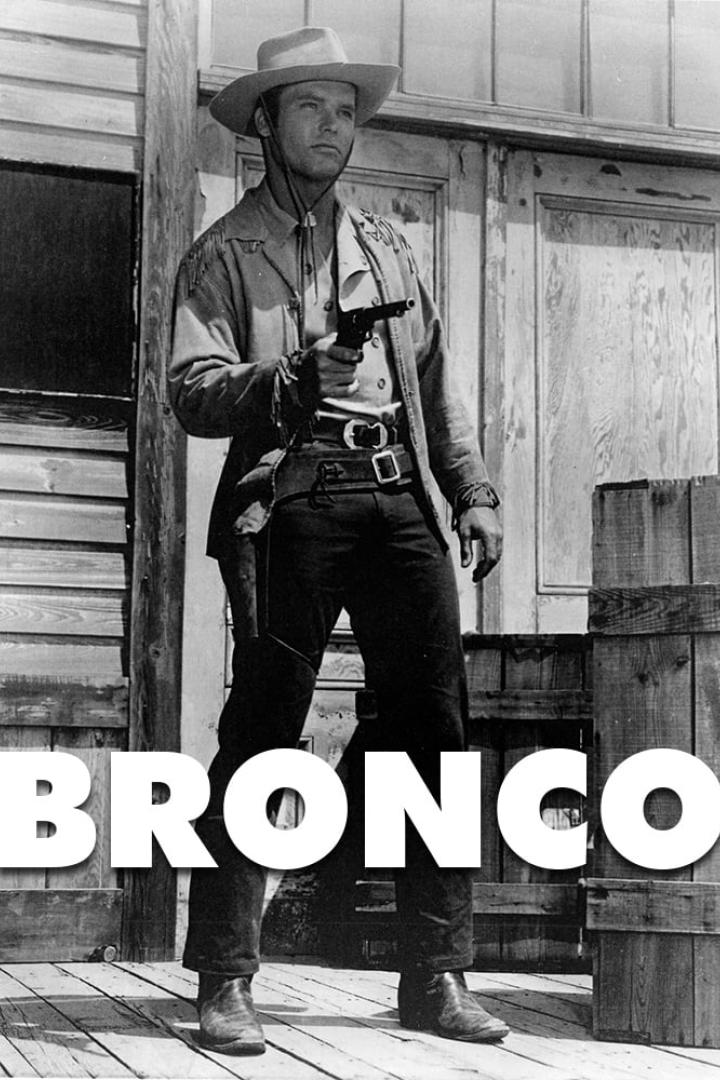 Ein Mann im Cowboyhut und mit Revolver vor einem Holzgebäude, im Vordergrund der Schriftzug „Bronco“.