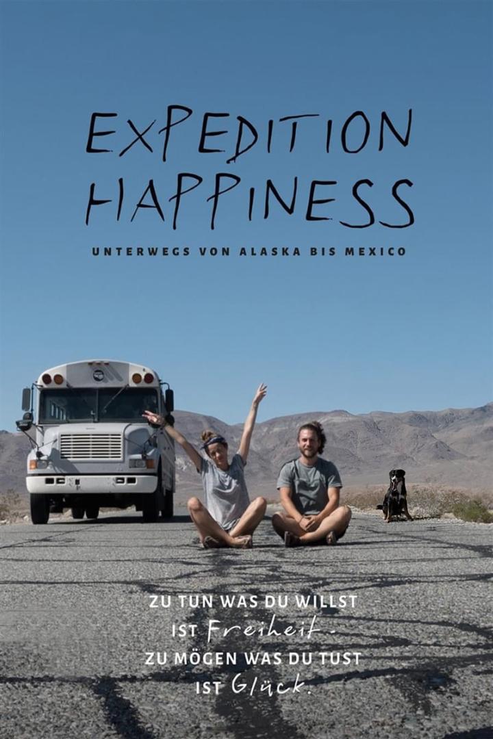 Ein Paar sitzt mit einem Hund und einem Bus auf einer Straße vor einer Bergkulisse; Titelbild von „Expedition Happiness“.