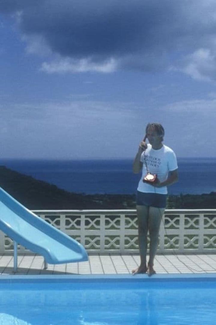 Ein Mann telefoniert mit einem roten Telefon am Pool mit Meerblick.