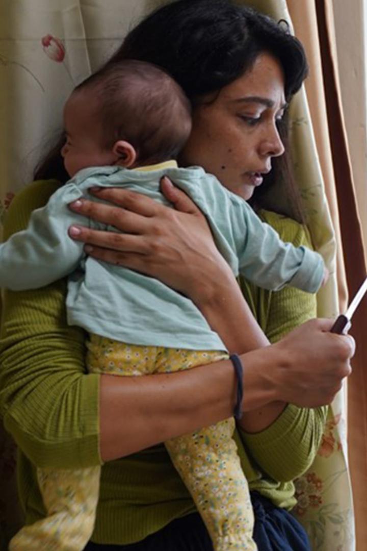 Eine Frau hält ein Baby im Arm und schaut auf ihr Handy.