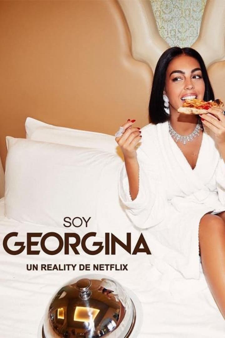 Georgina Rodríguez isst in einem weißen Bademantel Pizza auf einem Bett.