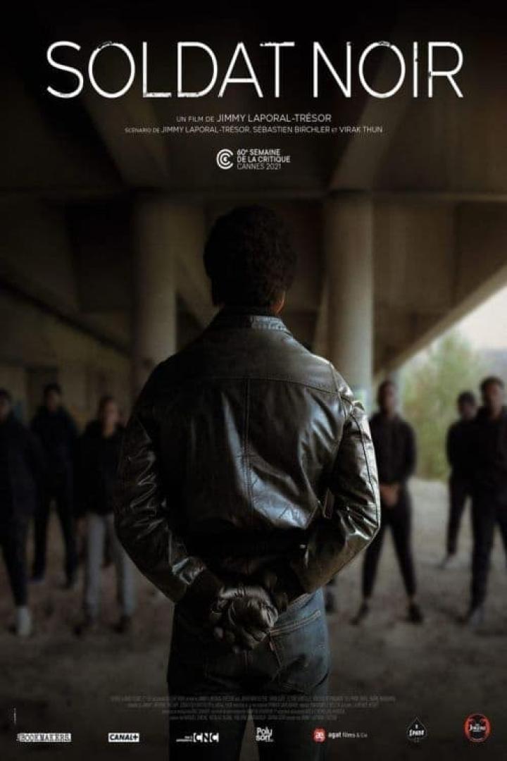 Ein Mann in Lederjacke steht vor einer Gruppe von Menschen, Plakat für den Film „Soldat Noir“.