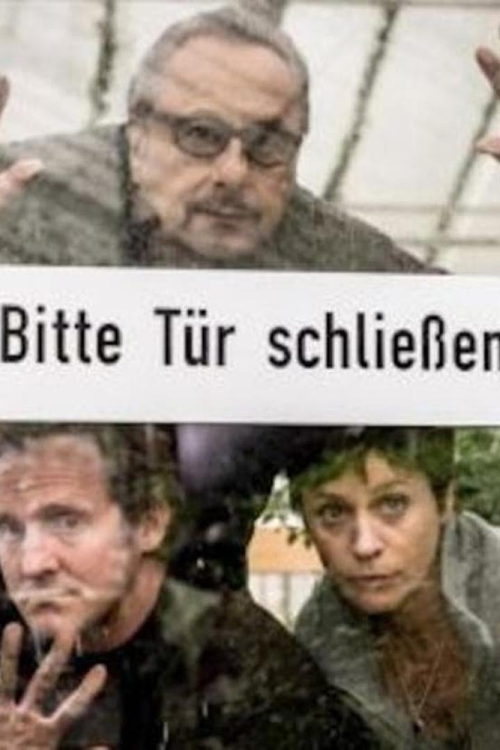Drei Personen stehen hinter einer Tür mit dem Schild „Bitte Tür schließen“.