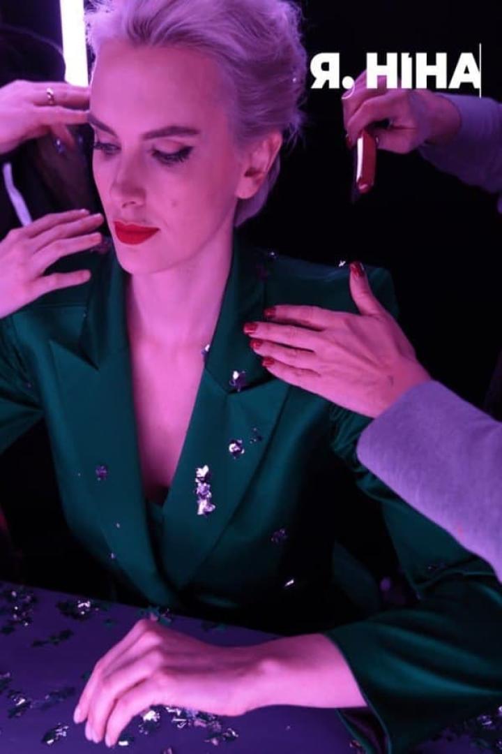 Eine Frau mit rotem Lippenstift und kurzem, blondem Haar trägt einen grünen Blazer.