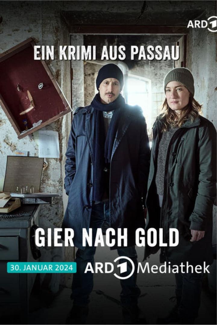 Zwei Kommissare stehen vor dem Poster für „Ein Krimi aus Passau: Gier nach Gold“.