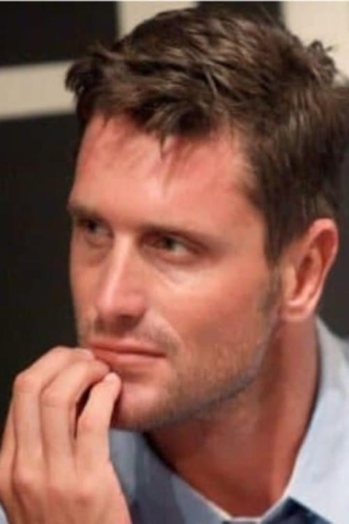 Ein Mann in einem hellblauen Hemd blickt nach links und berührt sein Kinn mit der Hand.